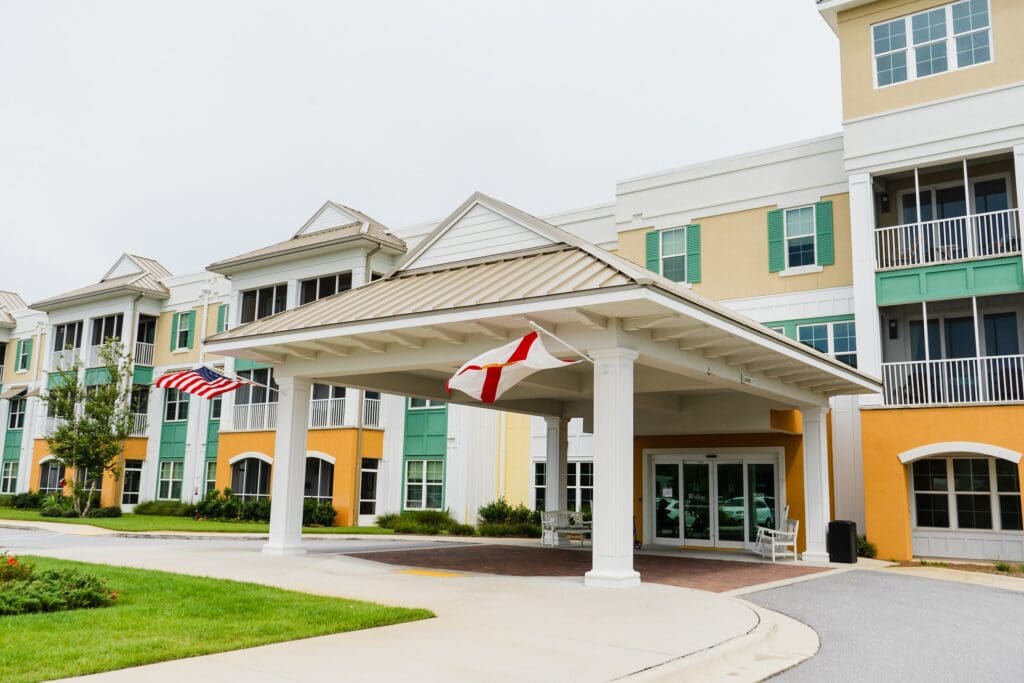 Welcoming entrance of a senior living community with vibrant colors, flags, and lush greenery, embodying an upscale lifestyle.