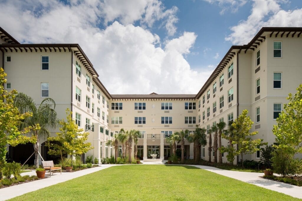 Elegant courtyard surrounded by modern senior living residences, featuring lush landscaping and bright, inviting architecture.