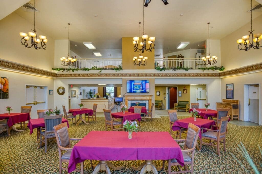 Spacious senior dining area with elegant decor, vibrant red tablecloths, and chandelier lighting, promoting a warm community atmosphere.