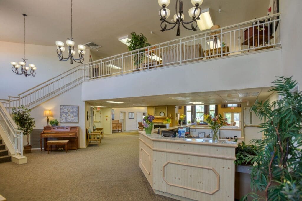 Welcoming lobby of a senior living community featuring elegant chandeliers, plants, and a reception desk adorned with flowers.