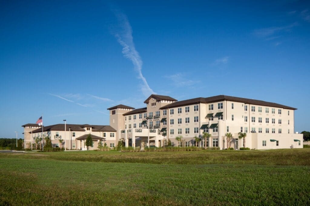 Upscale senior living community with elegant architecture, lush landscaping, and blue skies, promoting a vibrant lifestyle.
