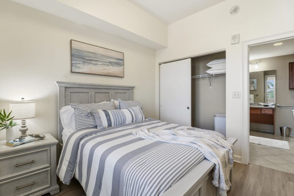 Chic senior living bedroom featuring modern decor, cozy bed with striped linens, and an adjoining bathroom.