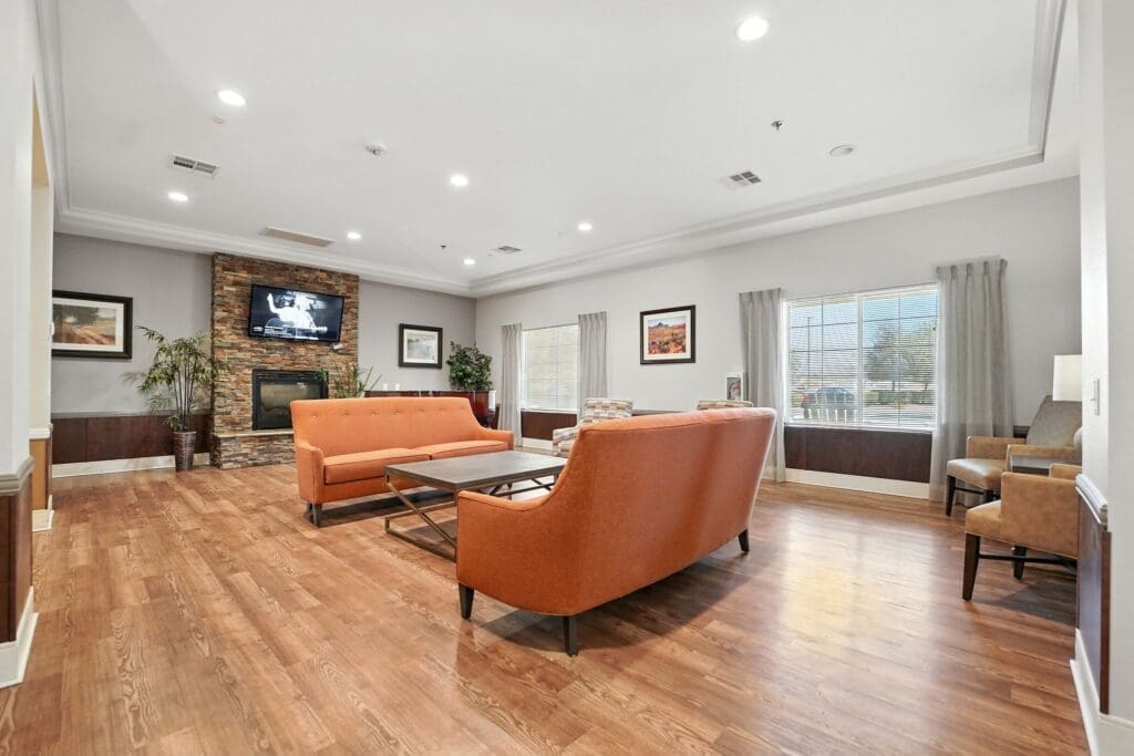 Welcoming lounge area featuring modern orange sofas, a stone fireplace, artwork, and natural light from large windows.
