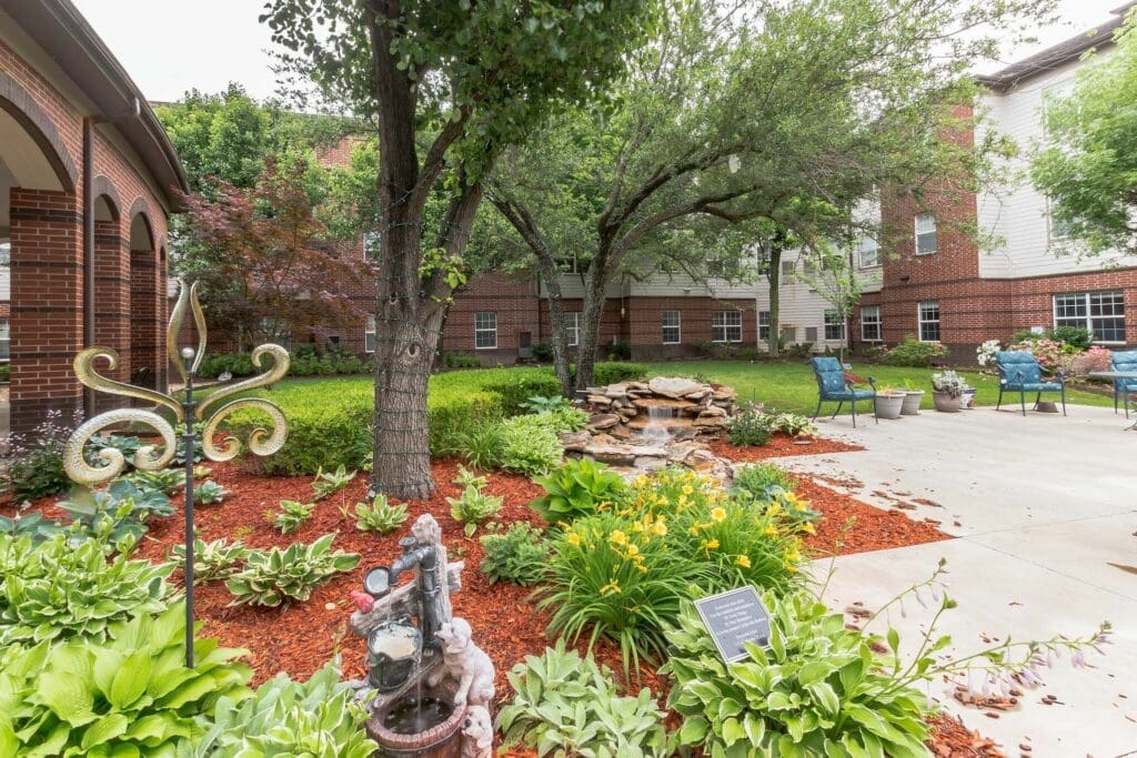 2022-05-26-HomeJab-154-11207128 - Grace Management Lush garden with a serene water feature, vibrant flowers, and elegant seating areas amidst a welcoming senior living community.