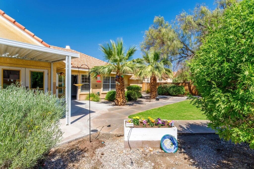 2022_LakeHavasu_EXT-Courtyard_77-2048x1365 - Grace Management Vibrant courtyard featuring palm trees, colorful flowers, and a sunny ambiance, enhancing the community's serene lifestyle.