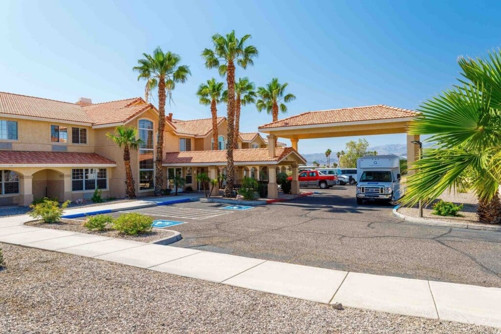 2022_LakeHavasu_EXT-Front_5-2048x1365 - Grace Management Exterior of a vibrant senior living community featuring palm trees, a welcoming entrance, and accessible parking spaces.