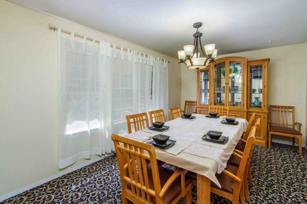 2022_LakeHavasu_INT-dining_36-2048x1365 - Grace Management Elegant dining room featuring a large wooden table set with black dishware, surrounded by cozy chairs and natural light.