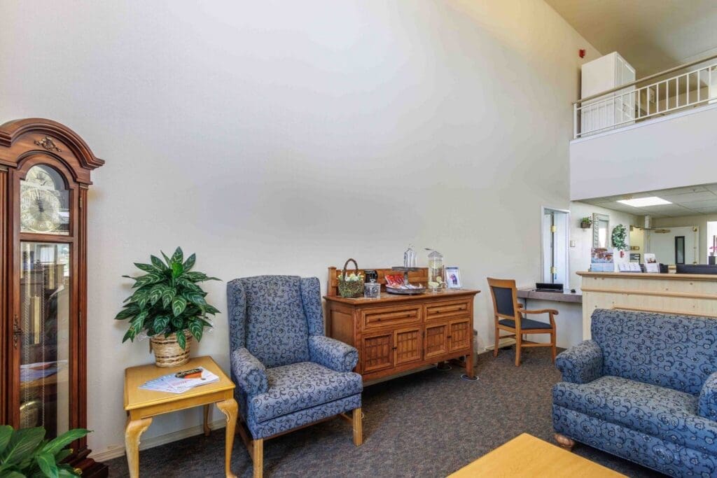 2022_LakeHavasu_INT-lobby_42-2-2048x1365 - Grace Management Inviting common area featuring plush blue armchairs, a wooden sideboard, and greenery, exuding warmth and comfort.