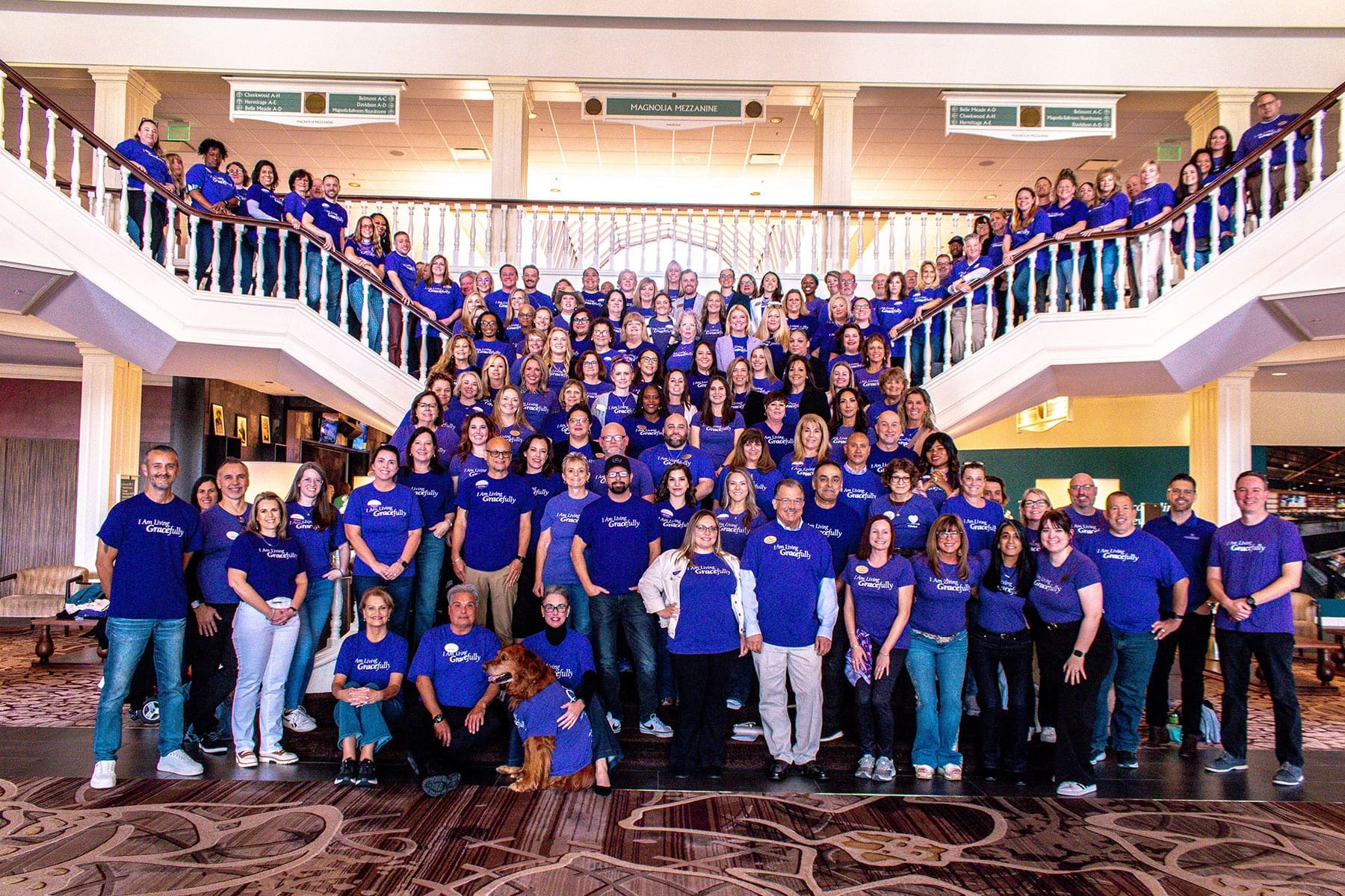 Team gathering in a spacious senior living community, smiles abound, all wearing vibrant purple shirts, showcasing unity and spirit.