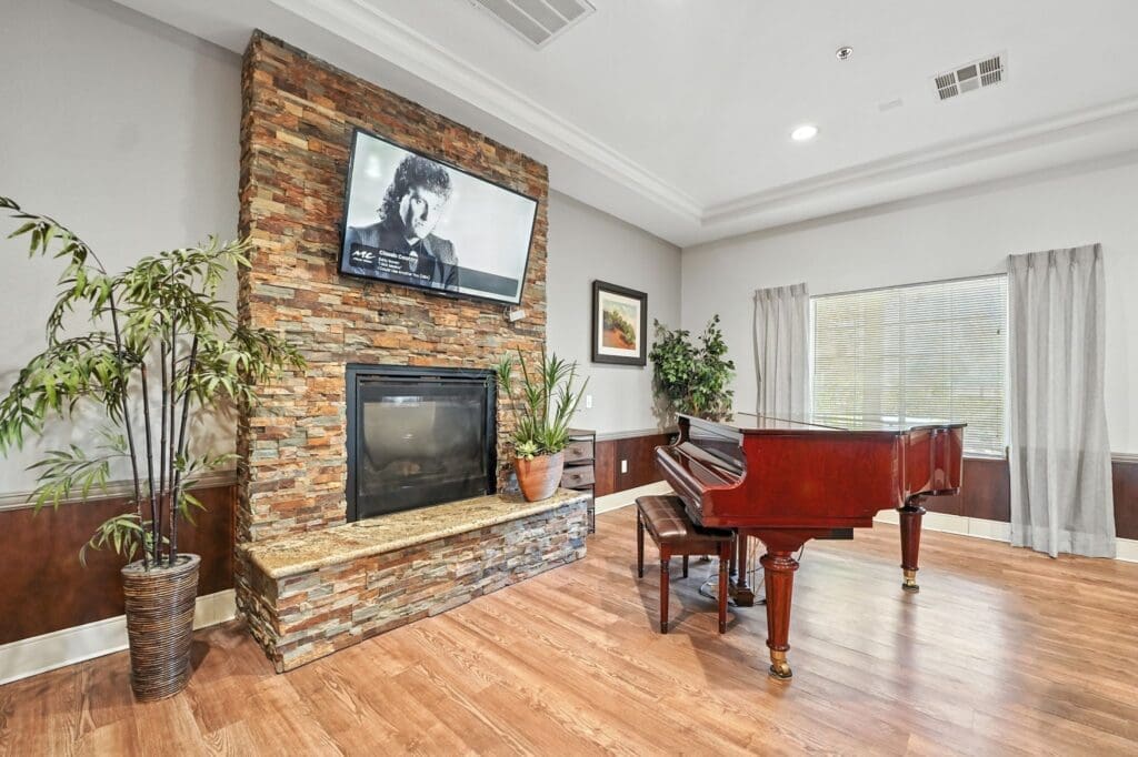 Elegant living room featuring a grand piano, stone fireplace, and lush greenery, creating a welcoming atmosphere.