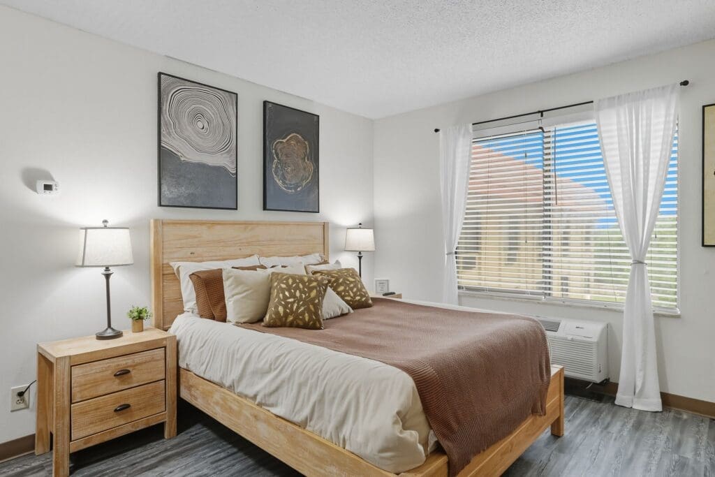 Cozy, elegantly decorated bedroom featuring a wooden bed frame, plush pillows, and bright natural light from large windows.