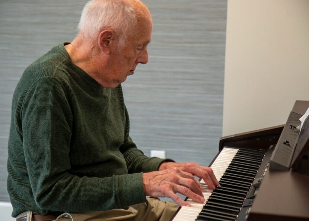 28-Large - Grace Management Senior man playing a digital piano, immersed in music, in a bright, modern setting.