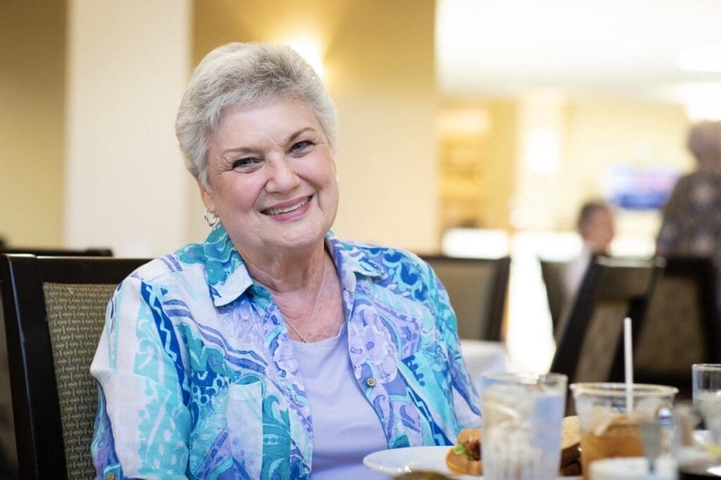 Smiling senior woman enjoying a meal in an inviting dining area, embodying a vibrant and joyful community atmosphere.