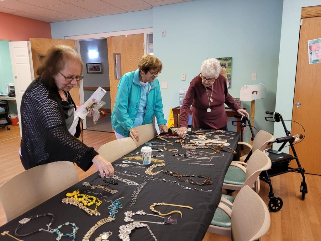 Three women engaging thoughtfully with a display of colorful jewelry in a bright, inviting activity space.