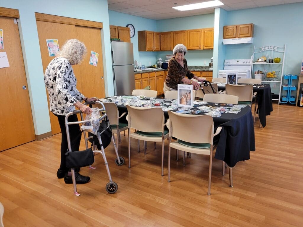 Two senior women engage in a crafting activity in a bright, inviting kitchen, surrounded by colorful supplies on tables.