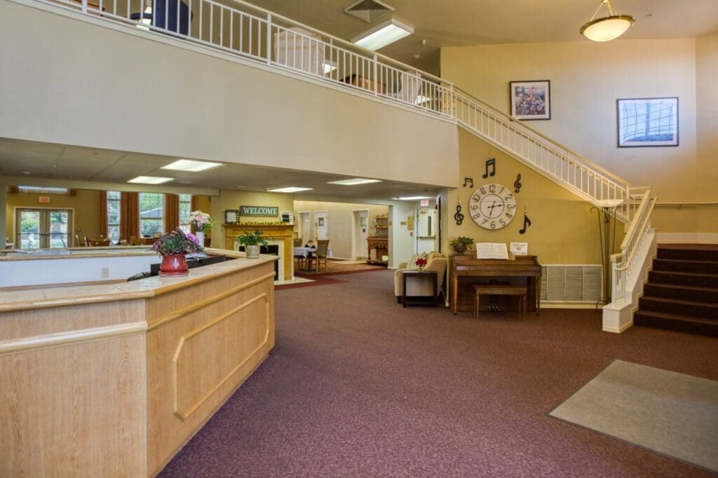 Welcoming senior living lobby featuring elegant decor, a grand piano, and a staircase leading to upper levels.