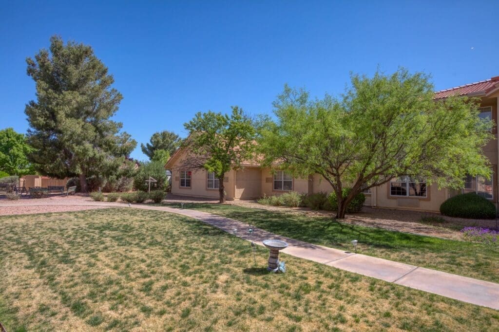 Lush green landscaping surrounds a charming senior living facility under a clear blue sky, inviting a vibrant lifestyle.