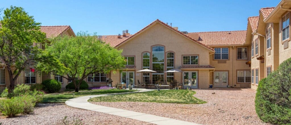 Elegant senior living community featuring a landscaped courtyard, patio seating, and vibrant foliage under a clear blue sky.