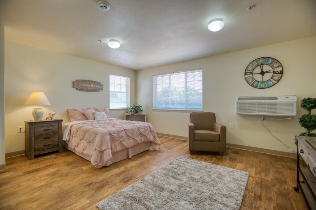 Elegant senior bedroom featuring soft pink bedding, cozy chair, warm lighting, and inviting decor.