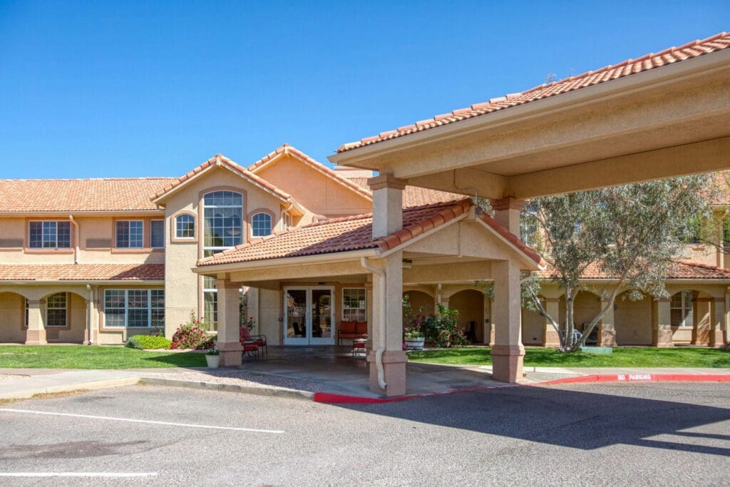 Welcoming entrance of a senior living community featuring upscale architecture and lush landscaping under a clear blue sky.