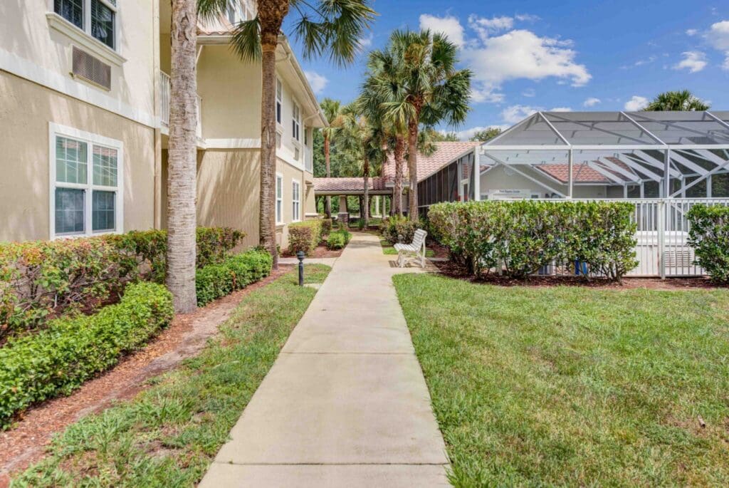 Lush landscaped pathway leading to a welcoming entrance, surrounded by palm trees and vibrant greenery in a senior living community.