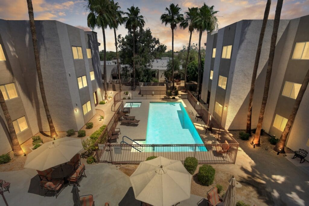 9160_E_Desert_Cove_Ave__Scottsdale__AZ_85260__USA-20220526212744 - Grace Management Upscale pool area surrounded by elegant buildings and palm trees, featuring lounge chairs and shaded seating for relaxation.