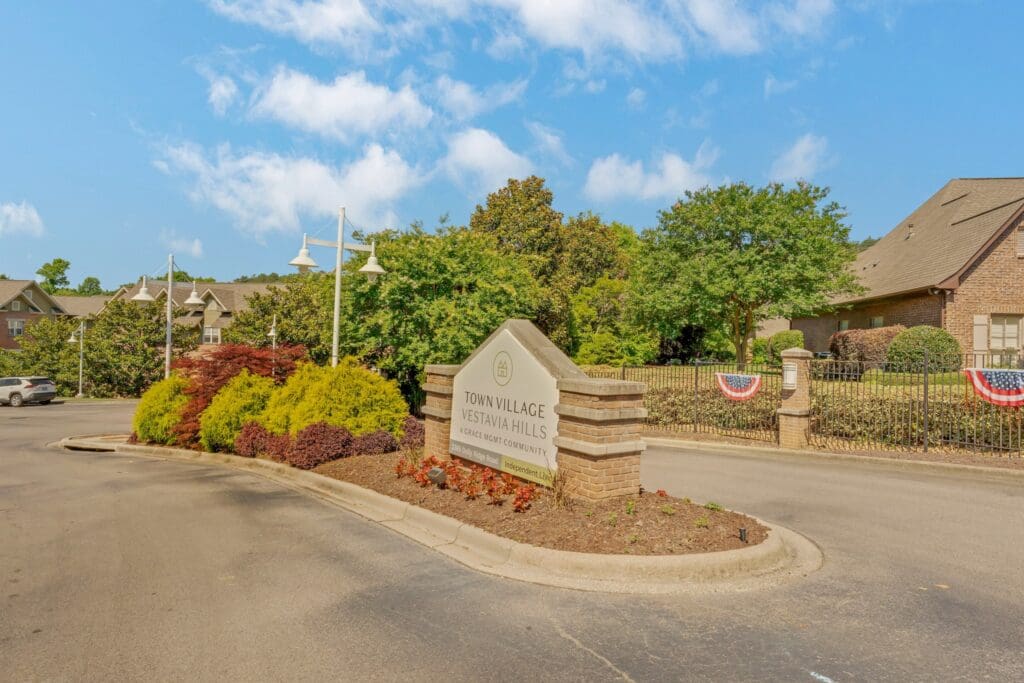 Welcoming entrance to Town Village Vestavia Hills, featuring lush landscaping and upscale amenities under a bright blue sky.