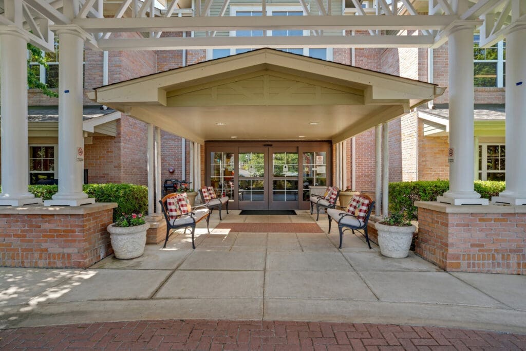 Welcoming entrance to a senior living community featuring stylish benches, potted plants, and elegant architecture.