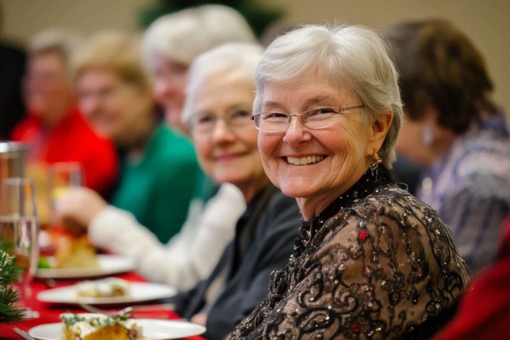 Cheerful senior woman in elegant attire enjoys a festive meal with friends at a warmly decorated dining table.