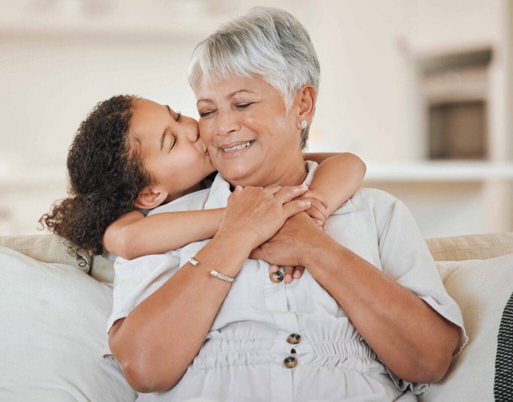 A joyful grandmother embraces her granddaughter, sharing a tender moment with smiles and love in a bright, welcoming living room.