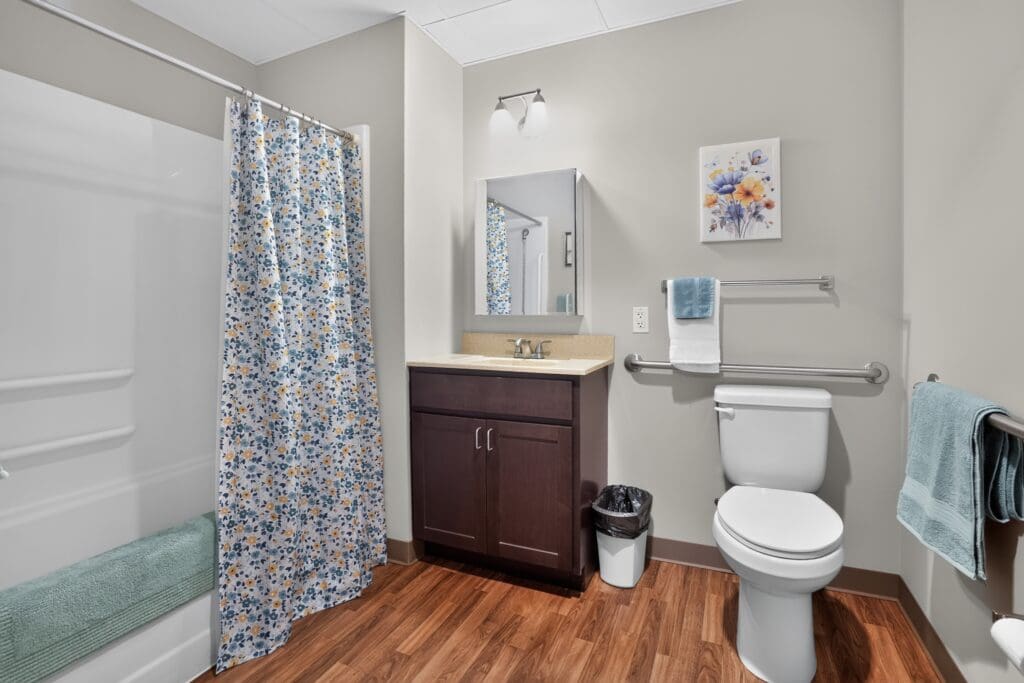 Elegant bathroom featuring upscale amenities, a floral shower curtain, modern fixtures, and a warm wooden floor.