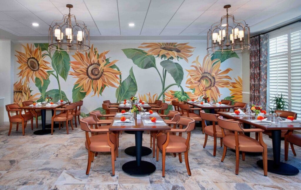 Bridgewater-Dining-Room-4-2048x1293 - Grace Management Elegant dining area with sunflower murals, stylish tables, and vibrant floral centerpieces for a warm, inviting atmosphere.