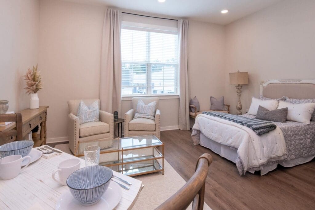 Elegant studio apartment featuring a cozy bed, stylish seating area, and delightful natural light from a large window.