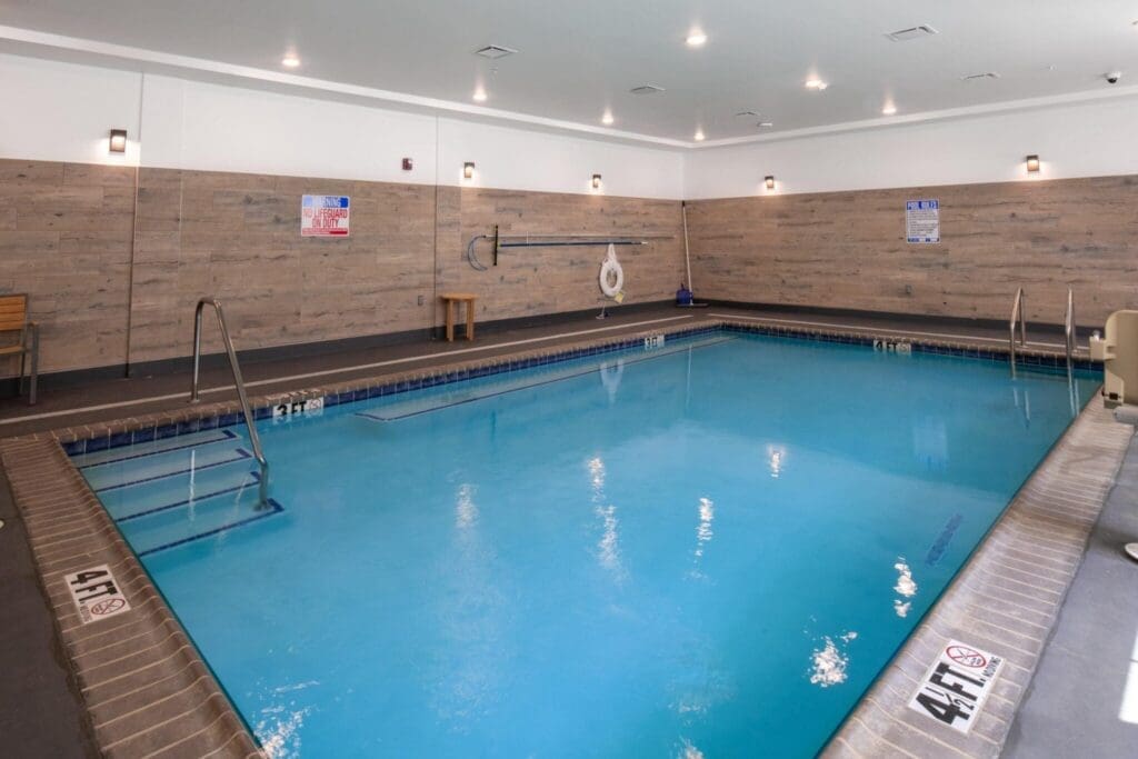 Indoor swimming pool with vibrant blue water, surrounded by elegant wooden paneling and accessible amenities.