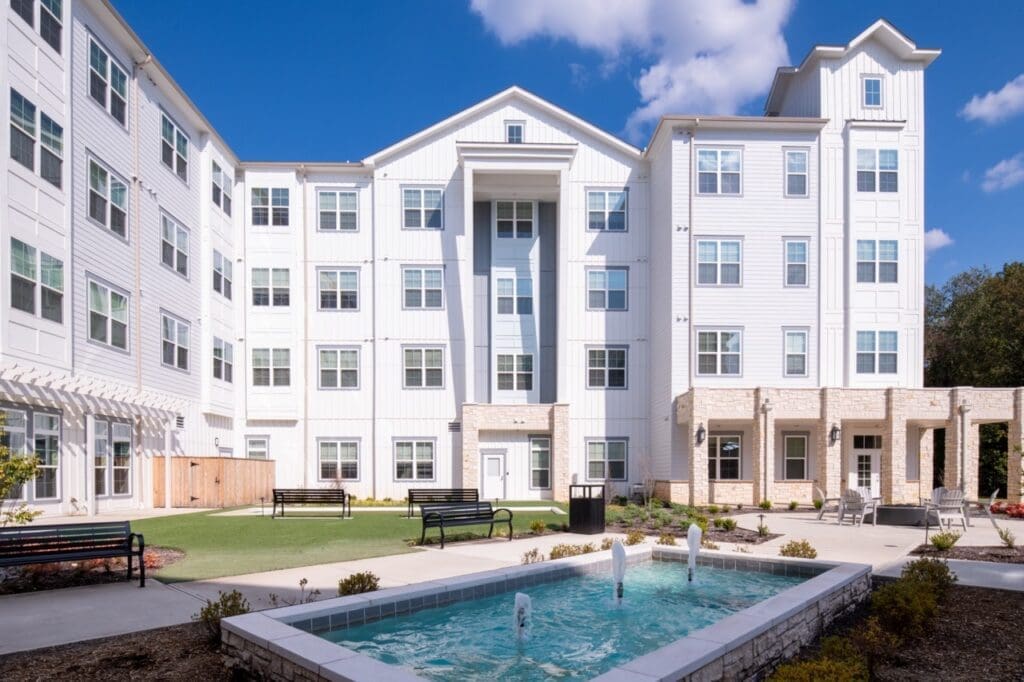 Modern senior living community featuring a serene courtyard, elegant water fountain, and inviting greenery.