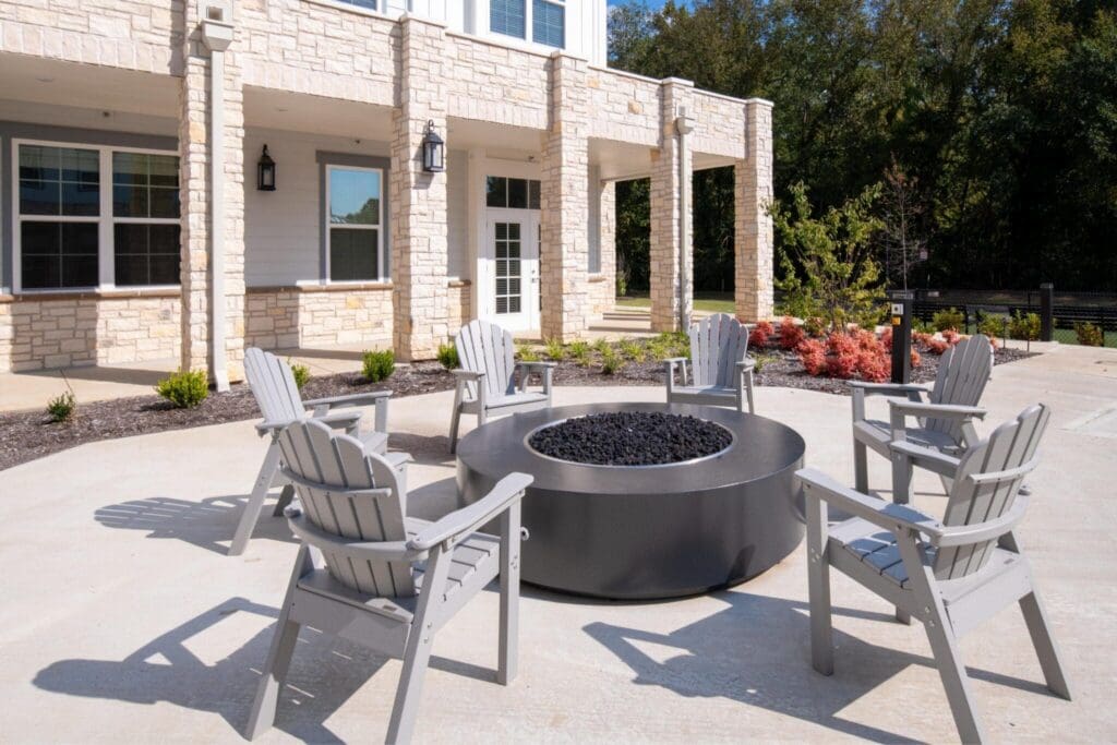 Charming outdoor seating area featuring gray Adirondack chairs surrounding a modern fire pit, accented by vibrant landscaping.