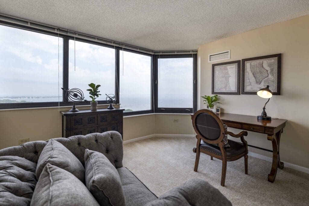 Bright, upscale living space featuring a cozy sofa, elegant desk, and panoramic windows showcasing serene waterfront views.