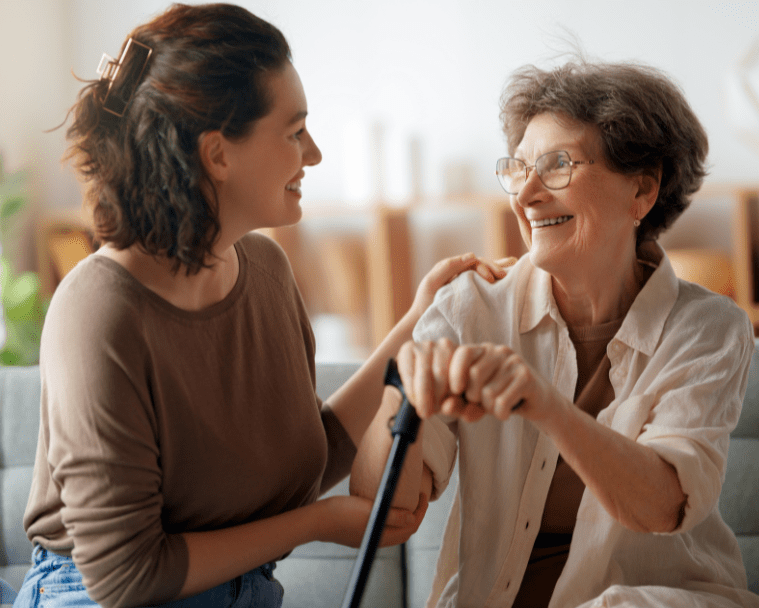A compassionate caregiver engages joyfully with an elderly woman, sharing smiles in a bright, welcoming living space.