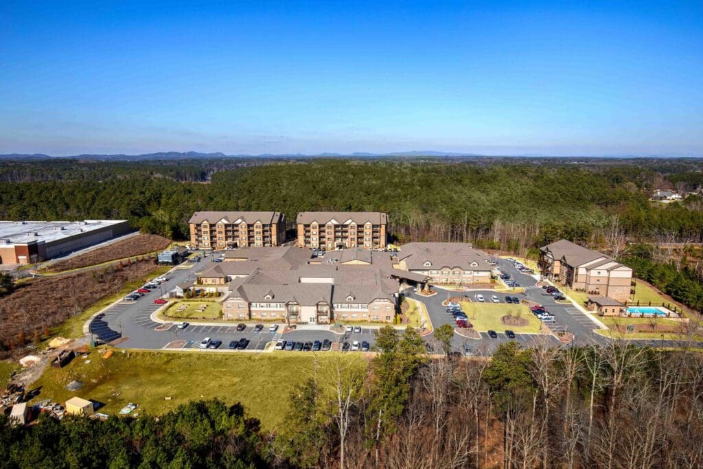 Aerial view of a senior living community featuring elegant buildings, ample parking, and lush surrounding greenery.