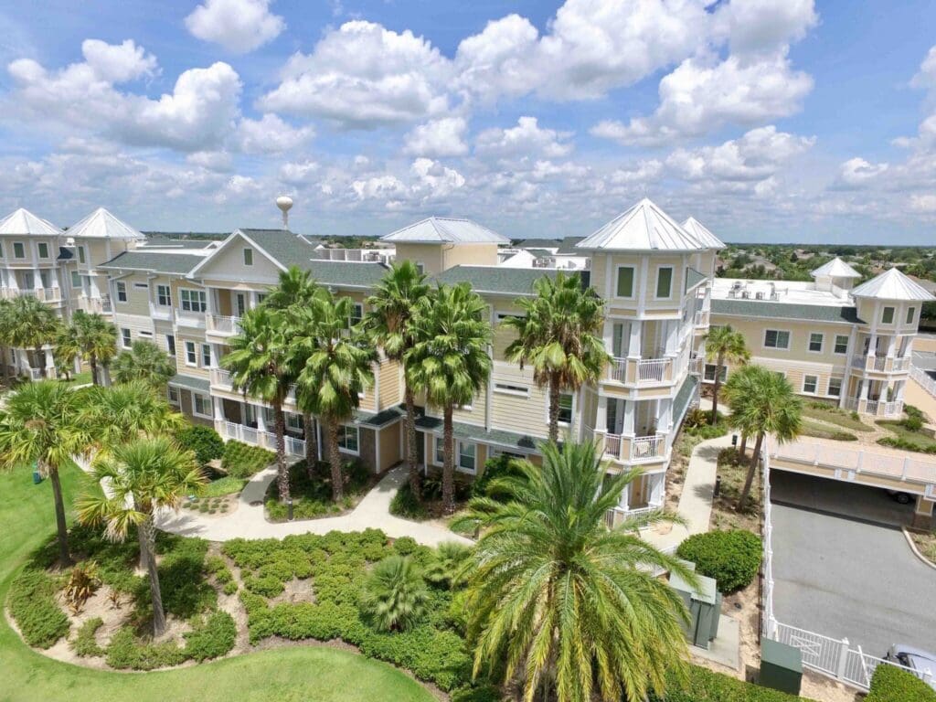 Spacious senior living community amid lush palm trees, featuring beautiful architecture under a sunny, blue sky.