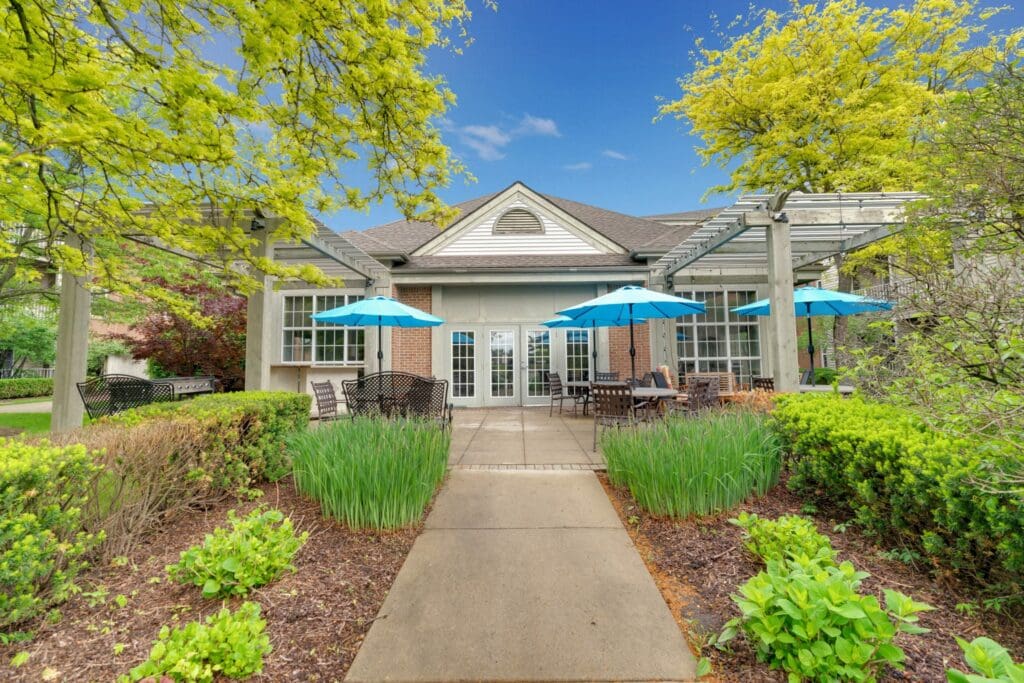 Charming outdoor patio with turquoise umbrellas, elegant seating, and lush greenery, inviting a vibrant lifestyle for residents.