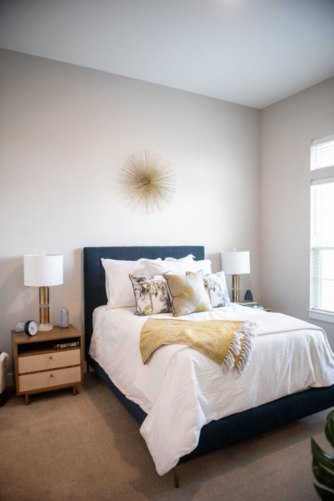 DSC1482-Large - Grace Management Bright, elegant bedroom featuring a plush bed with decorative pillows, stylish lamp, and warm gold accents.