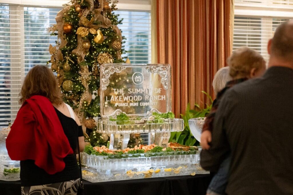 Guests enjoy a beautifully arranged buffet near a holiday-decorated tree and an ice sculpture, celebrating at the community event.