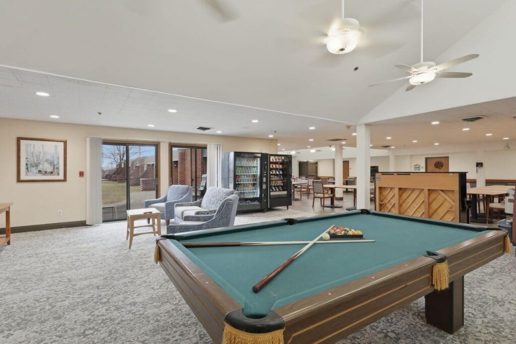 Entertainment_NorthgatePark - Grace Management Bright common room featuring a pool table, cozy seating, vending machine, and inviting views of the outdoor landscape.
