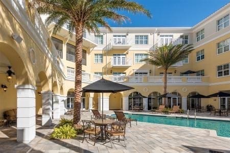 Exterior-Large - Grace Management Upscale courtyard featuring a sparkling pool, lounge chairs, and tropical palms under a clear blue sky.