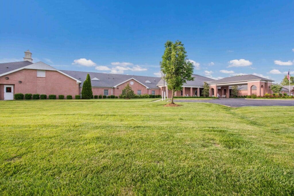 Inviting senior living community with well-maintained grounds, lush greenery, and elegant brick architecture under a clear blue sky.