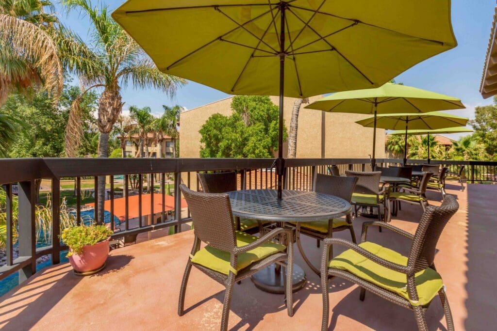 Final-Selects-303A5321-2048x1365 - Grace Management Stylish outdoor terrace with green umbrellas, wicker furniture, and a lush garden view, perfect for relaxation and community gatherings.