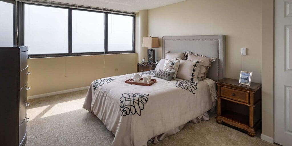 Elegant bedroom featuring a cozy bed with stylish decor, a wooden nightstand, and large windows offering ample natural light.
