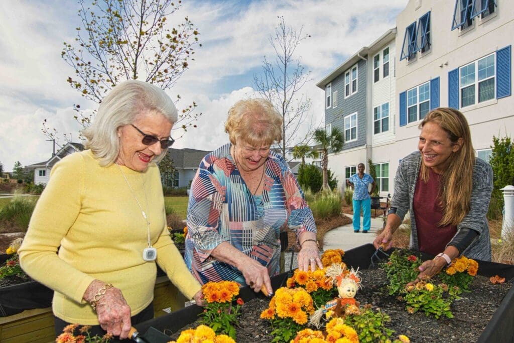 Garden-1-2048x1365 - Grace Management Seniors joyfully gardening together, planting vibrant marigolds in a landscaped courtyard with a friendly caregiver nearby.