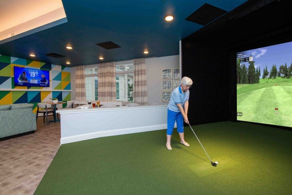 Golf-Lady-1-2048x1365 - Grace Management An active senior woman swings a golf club in a vibrant indoor golfing space, featuring rich colors and upscale decor.